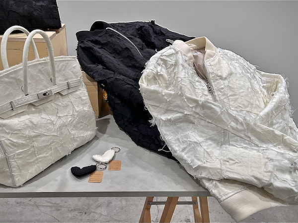 展示会で展示された作品の写真。テーブルの左右にマーキュリーが生地の制作を担当したバッグとブルゾン、中央にはハート型のチャームが置かれている。