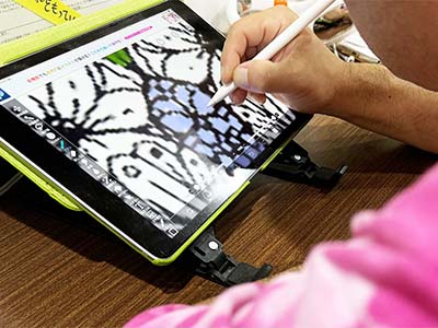 イラストの仕事の写真。タブレットとスタイラスペンを使い、ペイントソフト上で花の絵に着彩をしている様子。