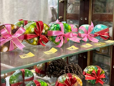 ハンドメイドの仕事の成果物の写真。透明でカラフルな、だ円形の手作り石けん(雑貨)がいくつか棚に並べられています。ビーズ状に小さく丸めた石けんを中に埋め込み、赤やピンクのリボンでラッピングされています。