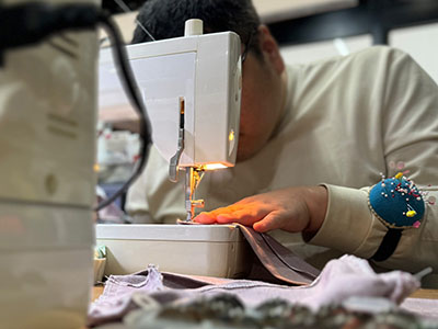 縫製の仕事の写真。服やバッグを布から作り出す作業。型紙に合わせて裁ち鋏で裁断した生地を、ミシンを使って縫い合わせている様子。