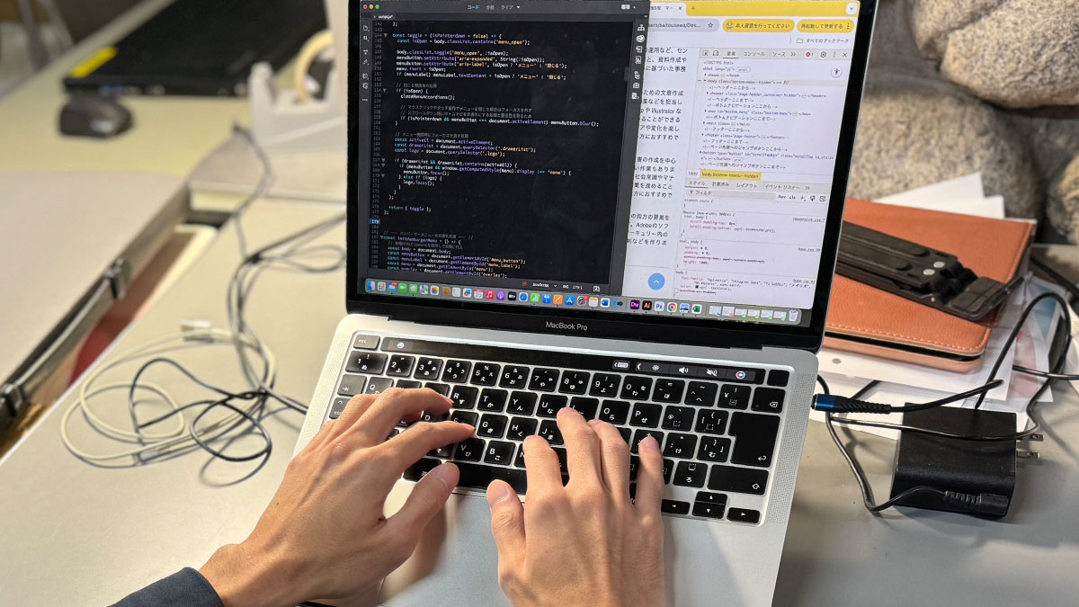 PC作業の仕事の写真。ノートパソコン上でAdobe社のDreamweaverというソフトを使ってコードを打ち込み、ウェブサイトを作成している様子。
